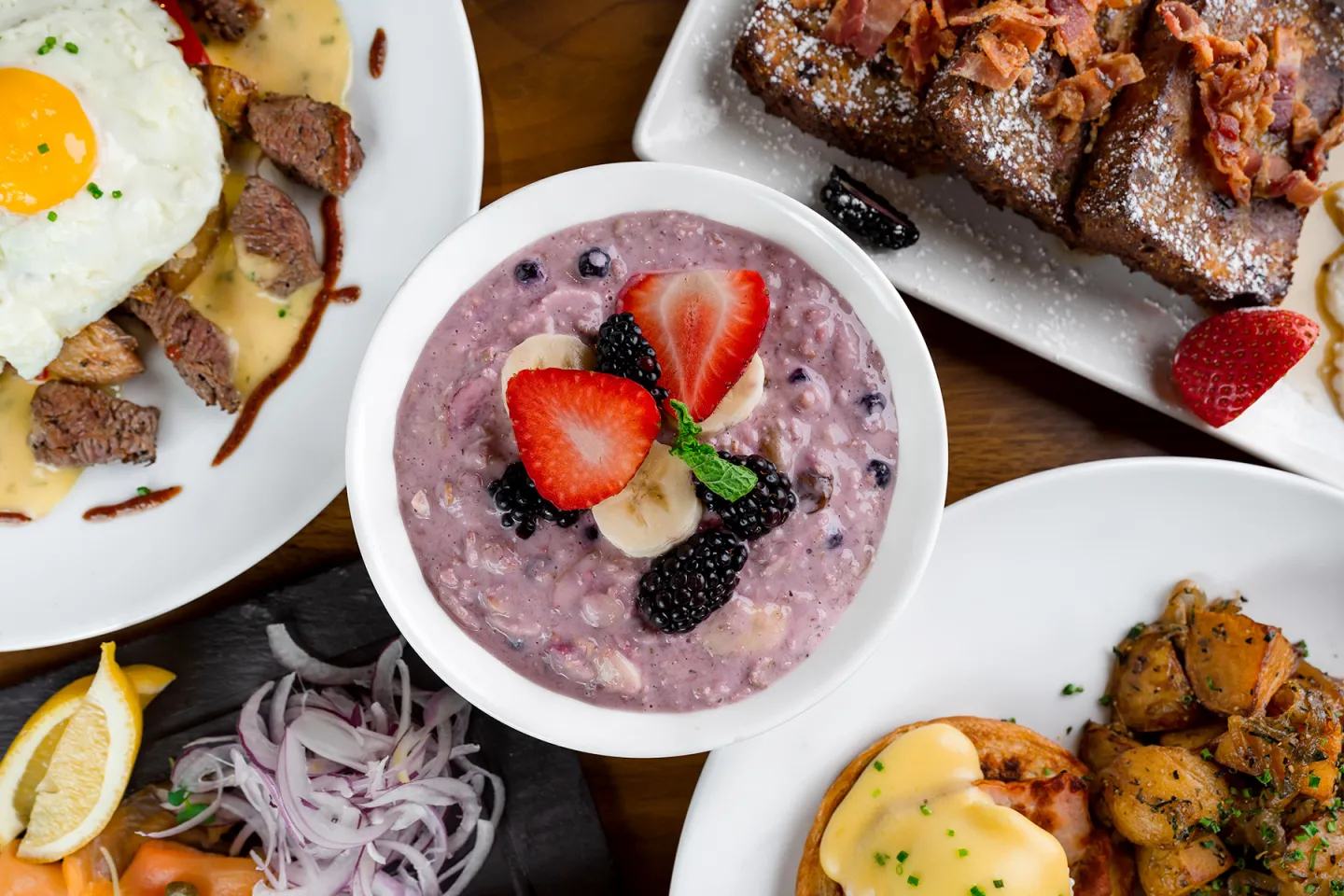 Assorted breakfast dishes including berry oatmeal and eggs with hollandaise.