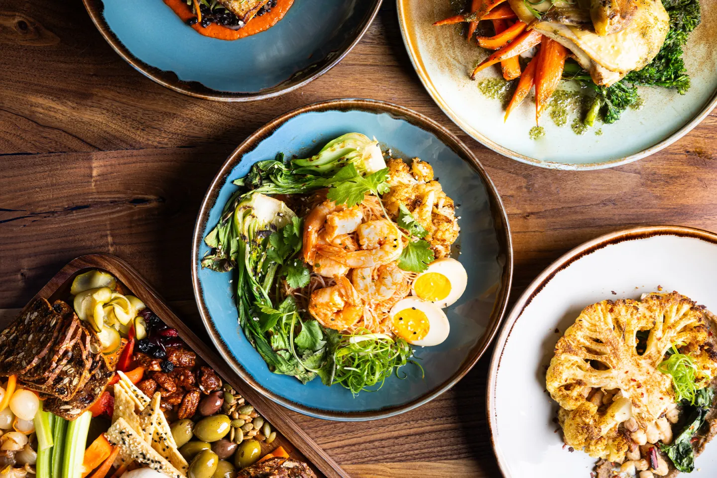 Assorted plates of colorful, vibrant meals on a wooden table.