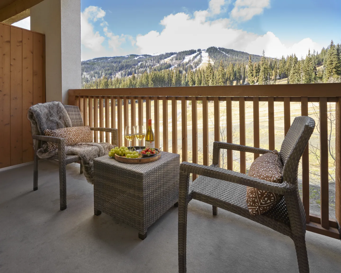 A hotel balcony with two chairs and a table looks over a resort mountain view