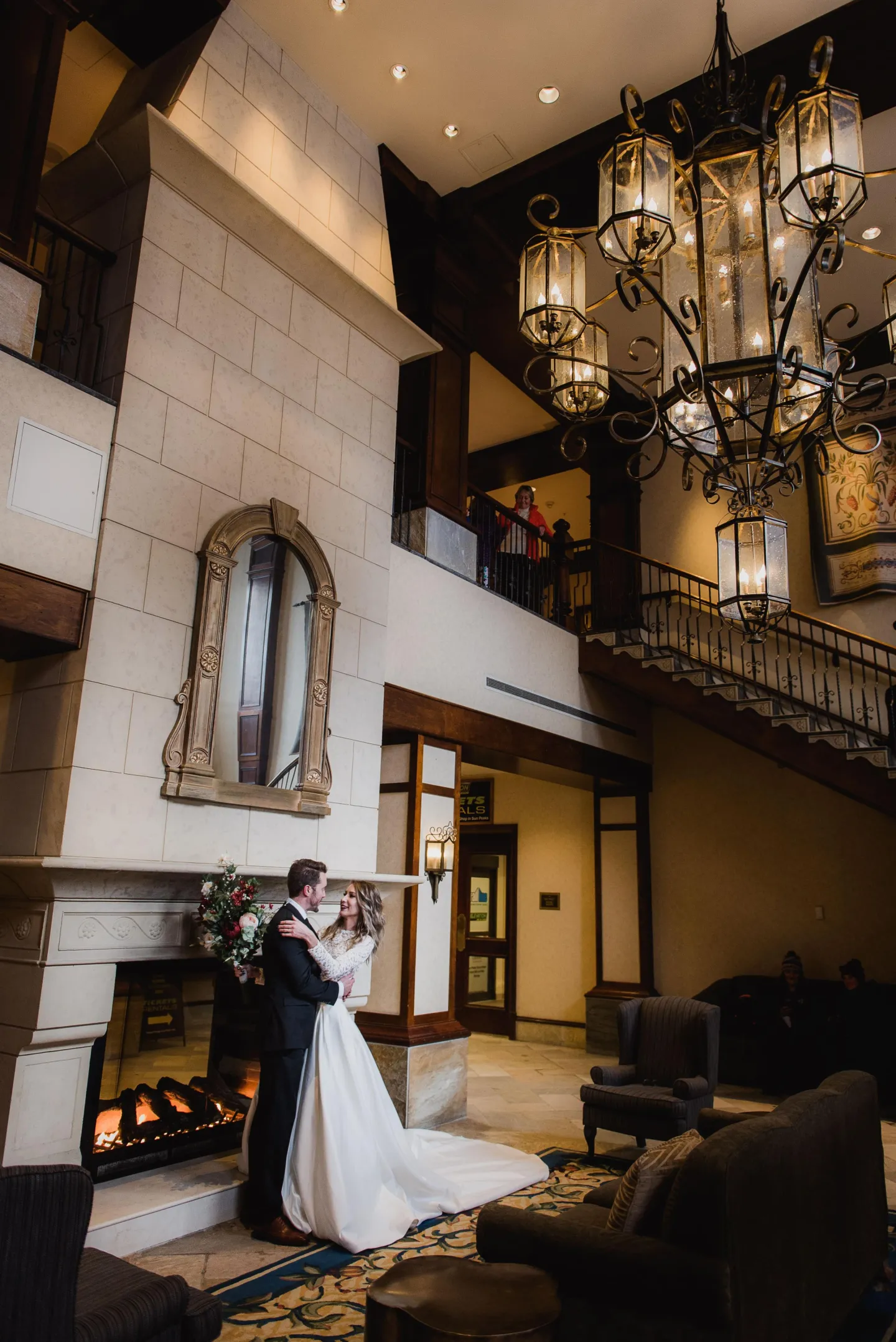 A bride and groom stand by a fireplace in a grand hotel lobby