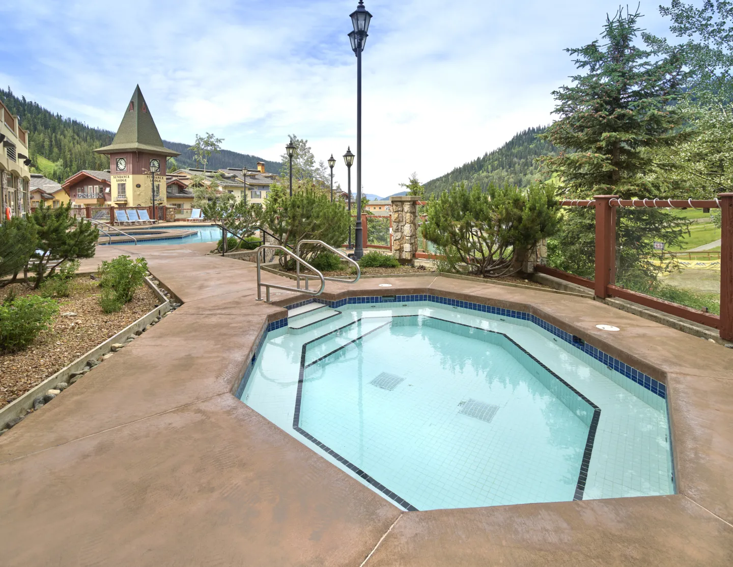 A view of an outdoor hot tub in summer with a resort and mountains in the background