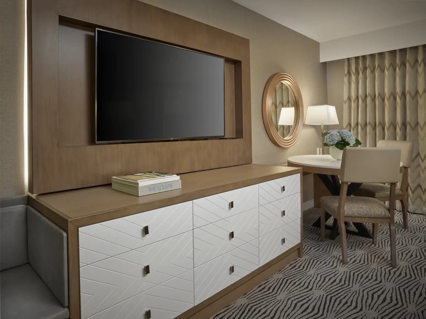 A flat screen tv above a hotel dresser surrounded by traditional furnishings