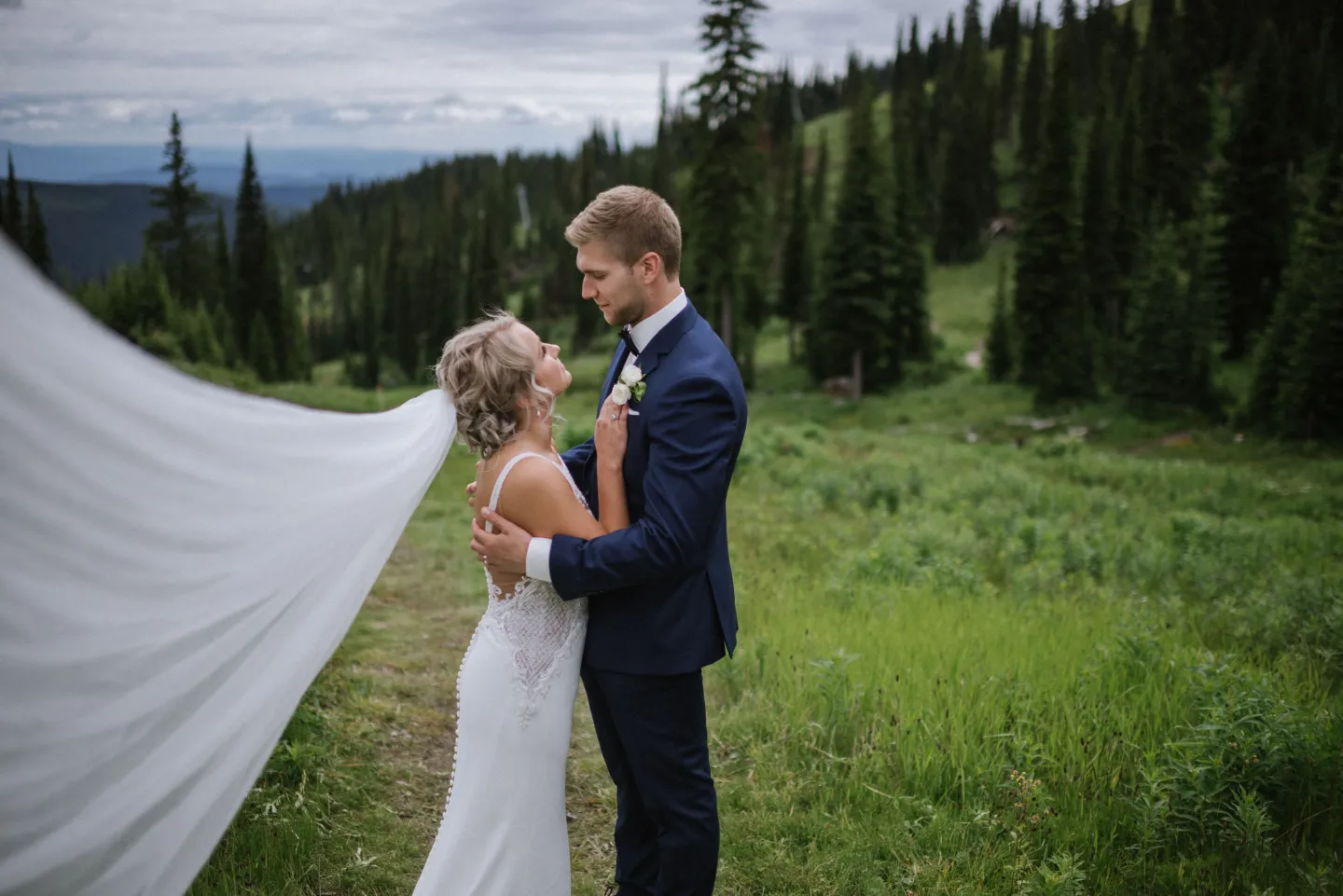 A bride and a groom pose for a photo on a grassy mountain