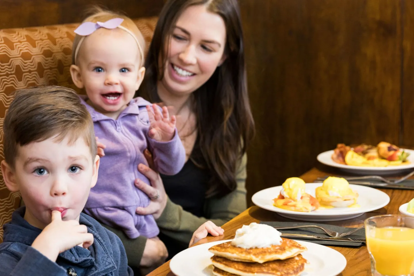 a woman and two kids at a table with breakfast food smiling at the camera