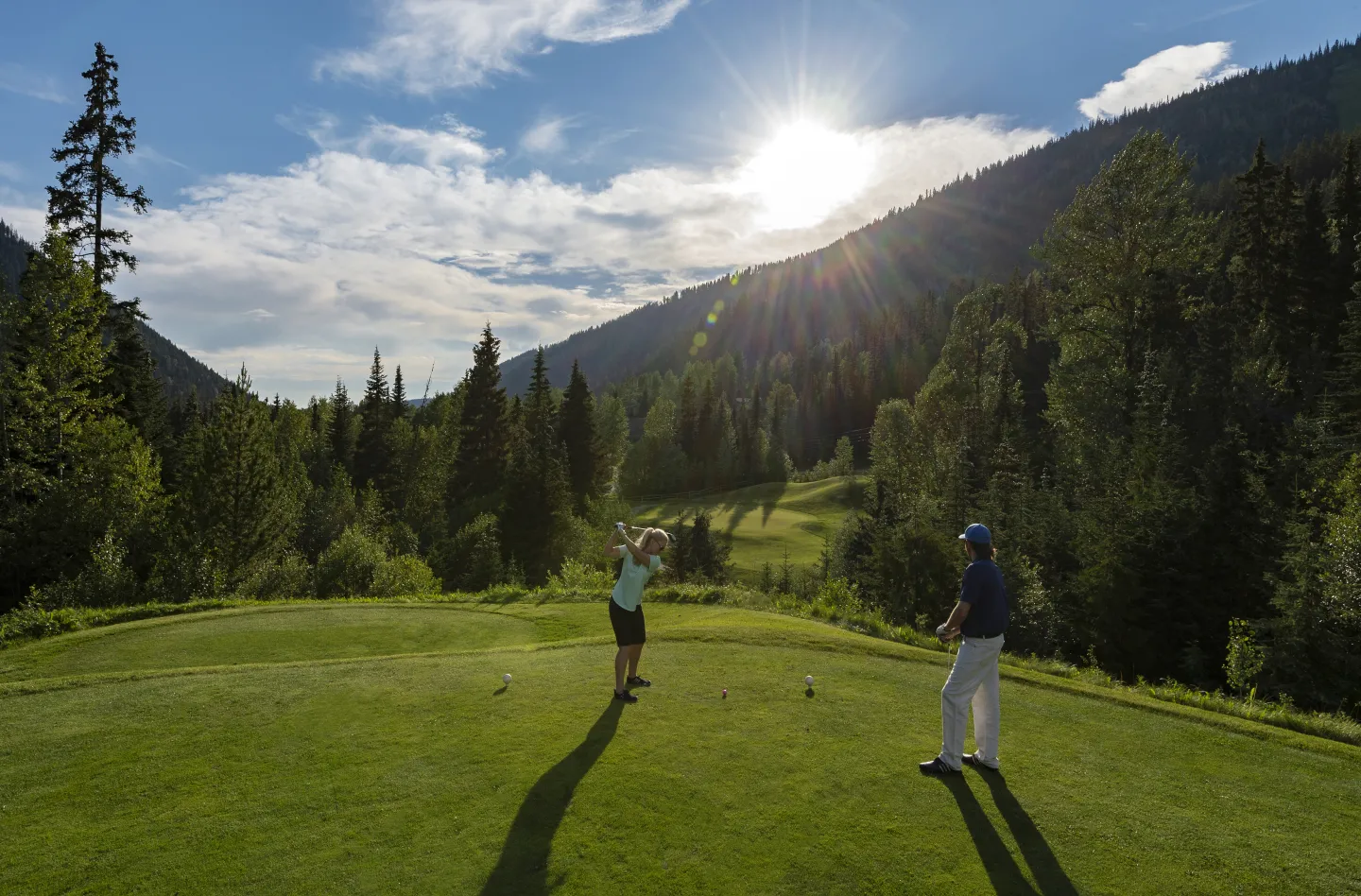 Two golfers on the green with the sunset in the valley