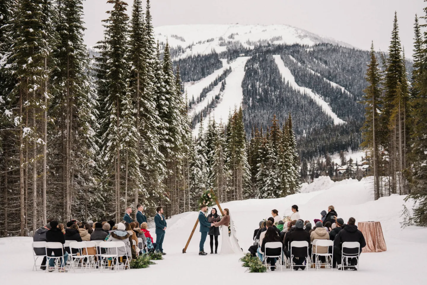 Bride and Groom at the alter in a field of snow with people sitting facing them and mountain views