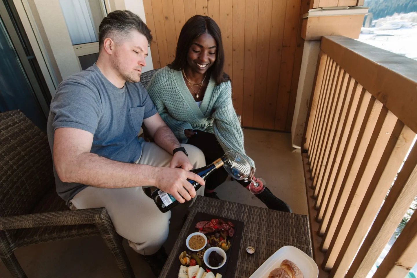 Two people on a balcony pouring wine and smiling