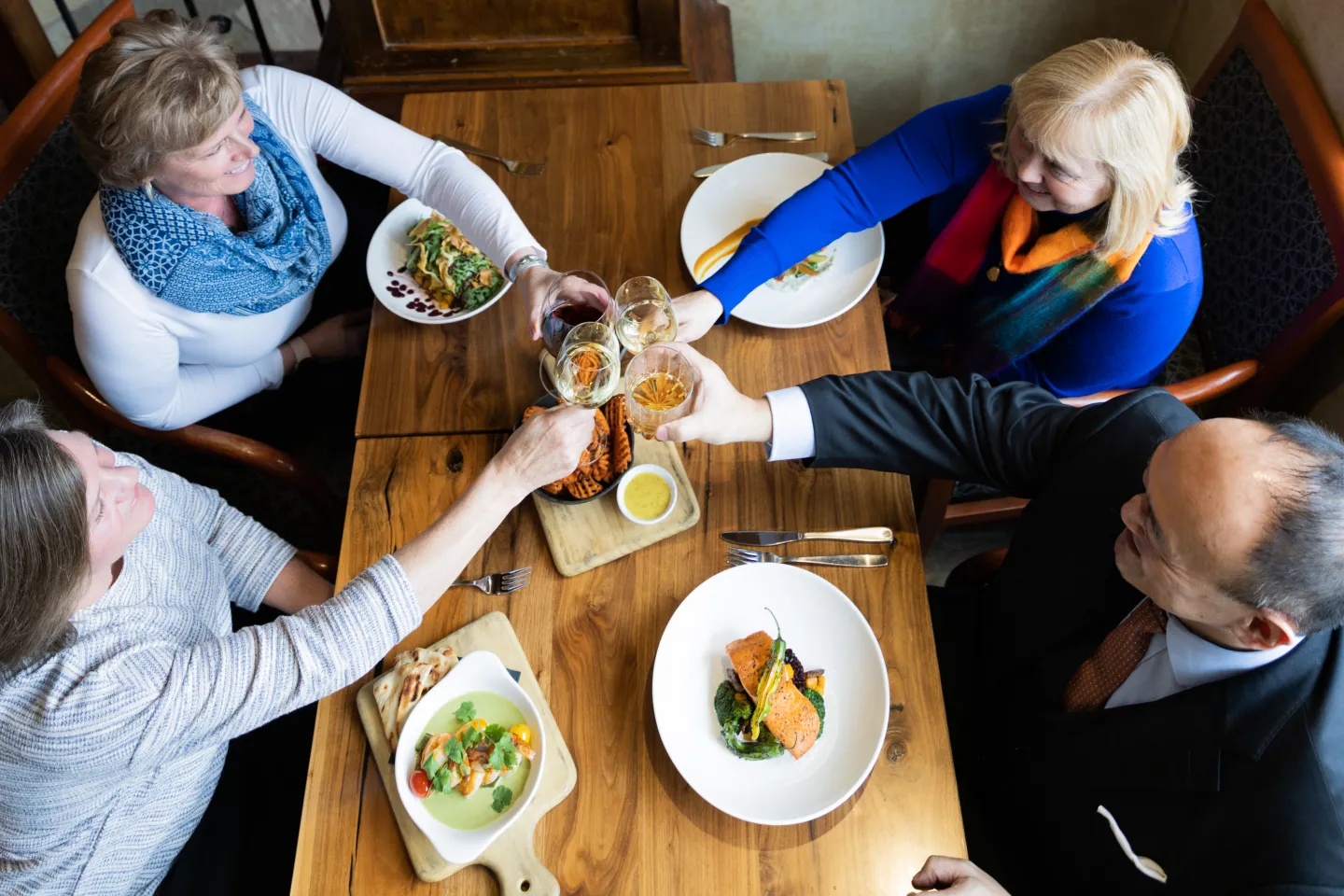 Four people cheering at a table with plated food.