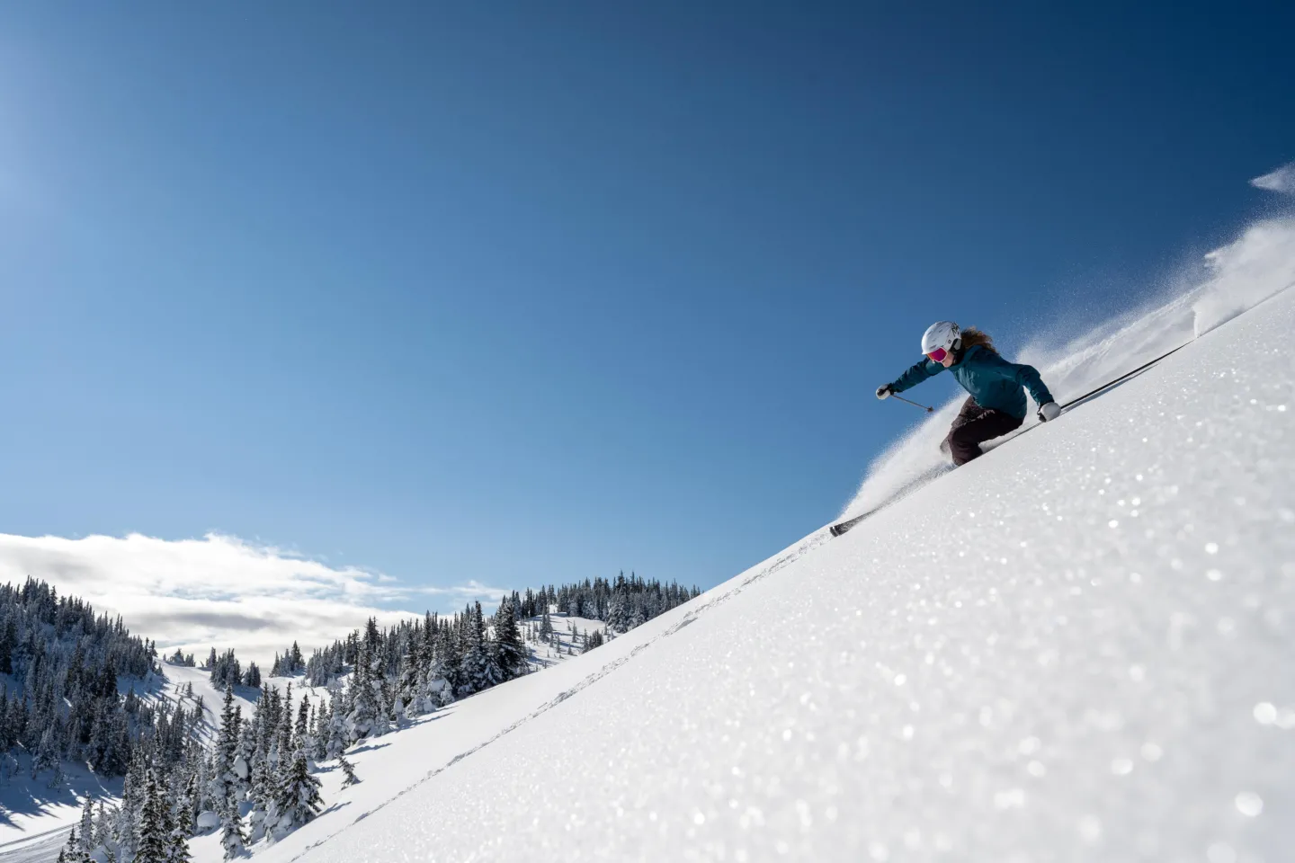Skier riding down a trail in powder on a bluebird day