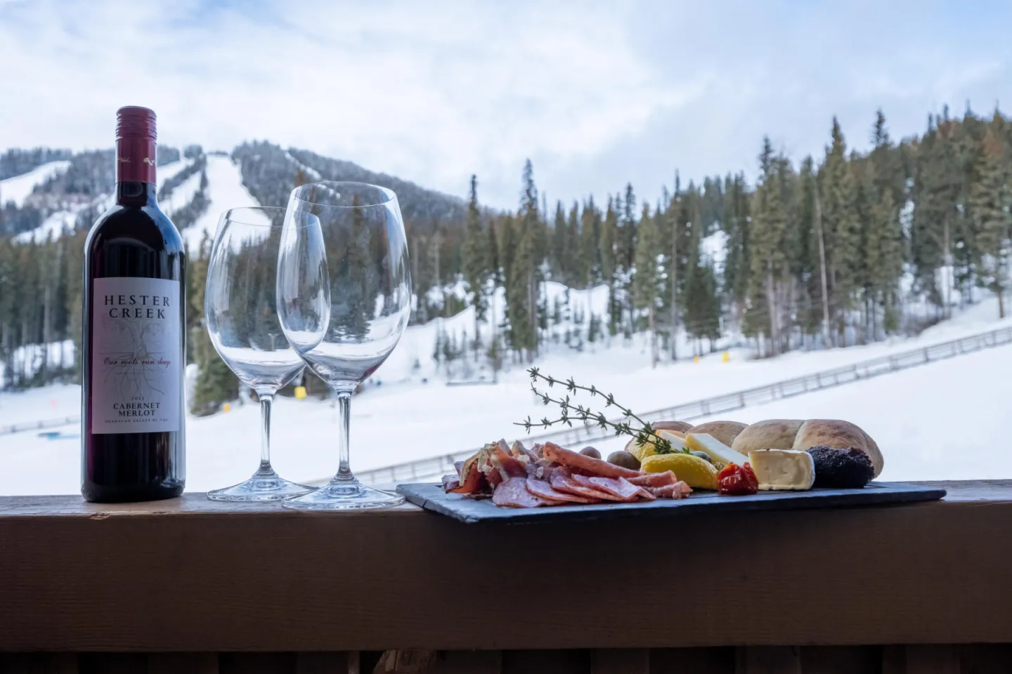 A bottle of wine and charcuterie board placed on a table with mountains in the background