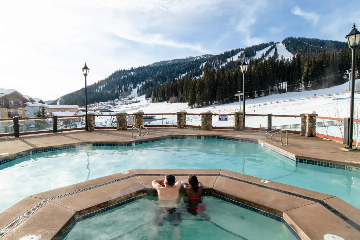 Two people in a pool looking out to the ski hill with mountain views