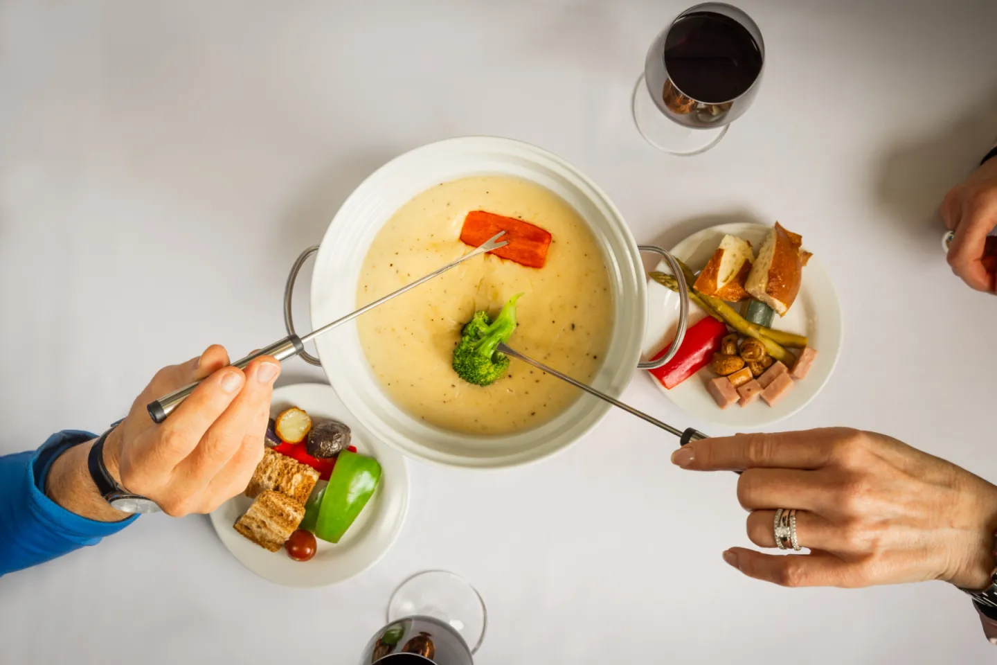 Fondue pot with people dipping vegetable in cheese