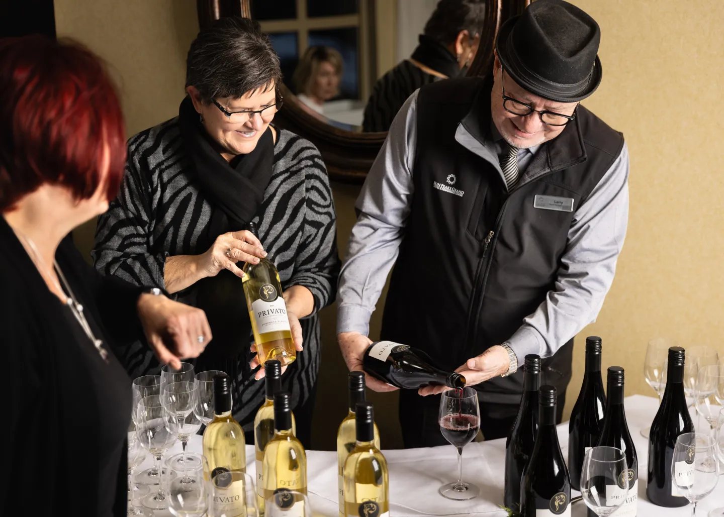 Three people standing around a table full of wine and pouring glasses