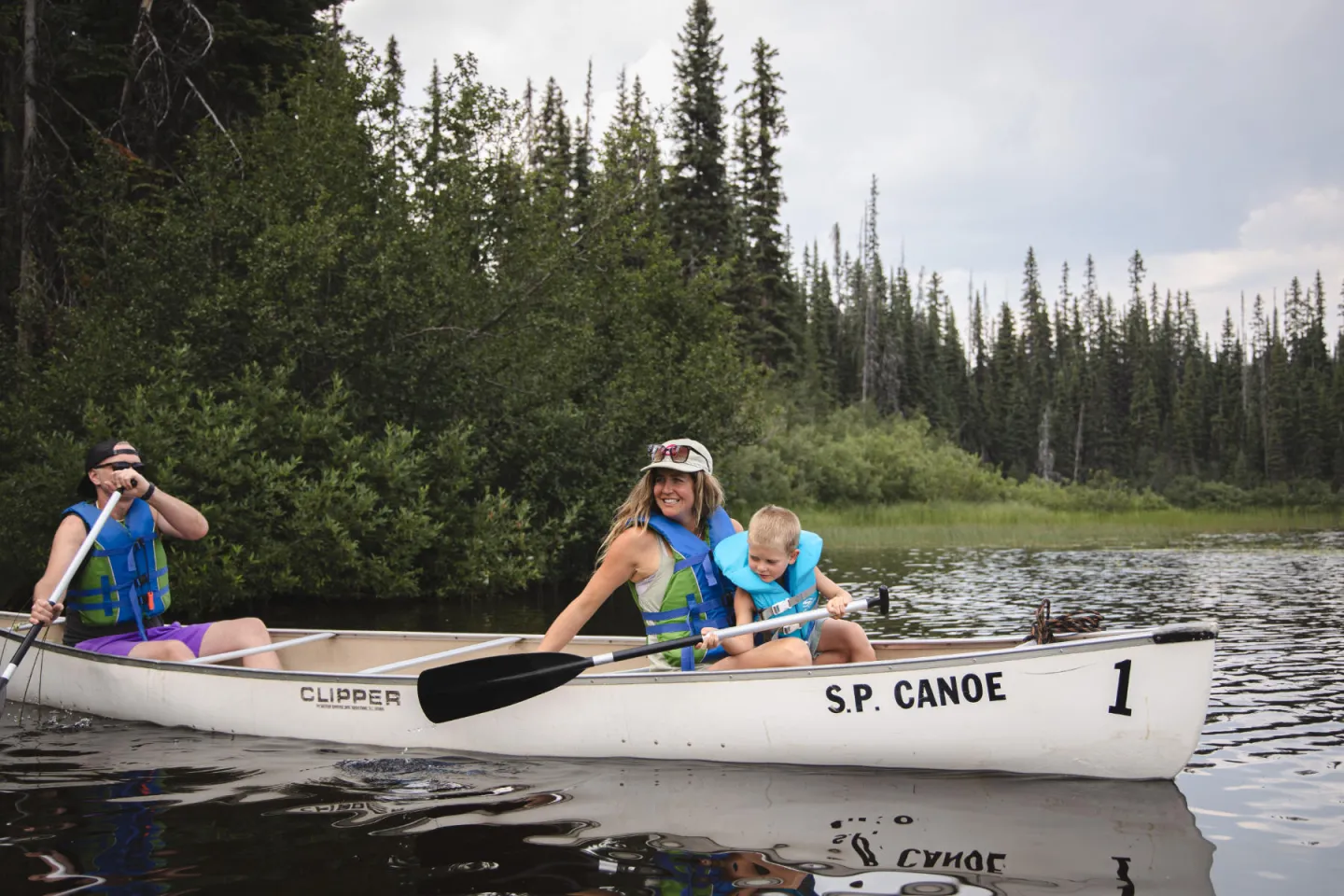 Two adults and a child in a canoe on the water with trees behind them