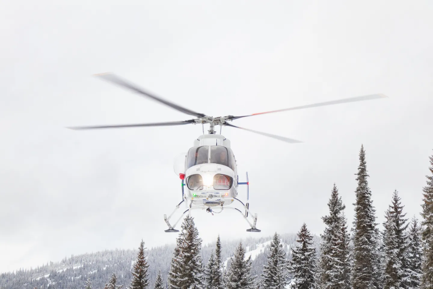 A helicopter flying above trees with a white sky in the background