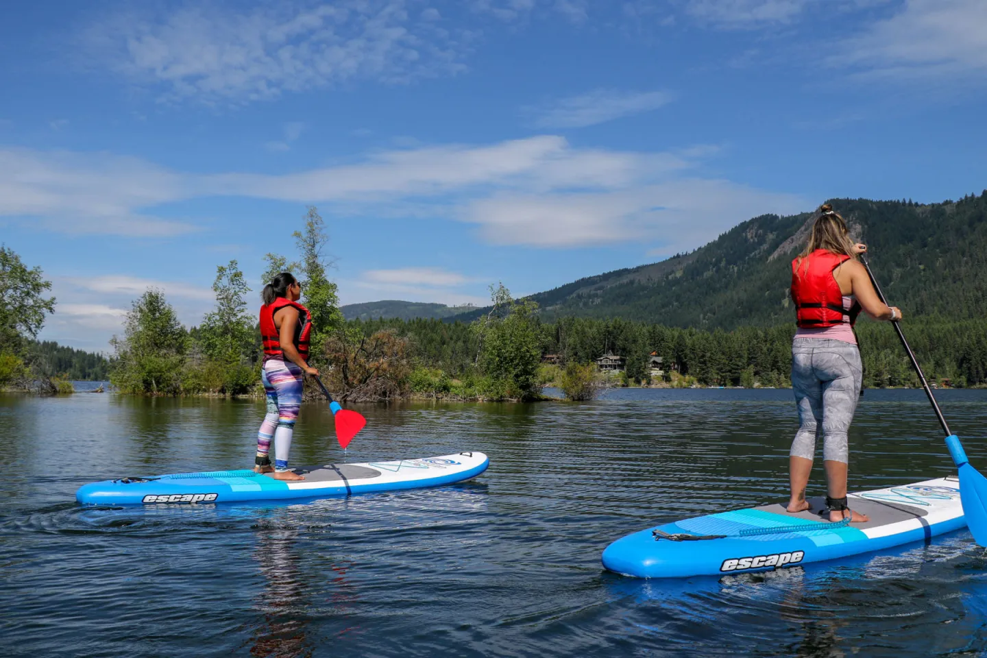Two women paddleboarding on a lake with mountain views