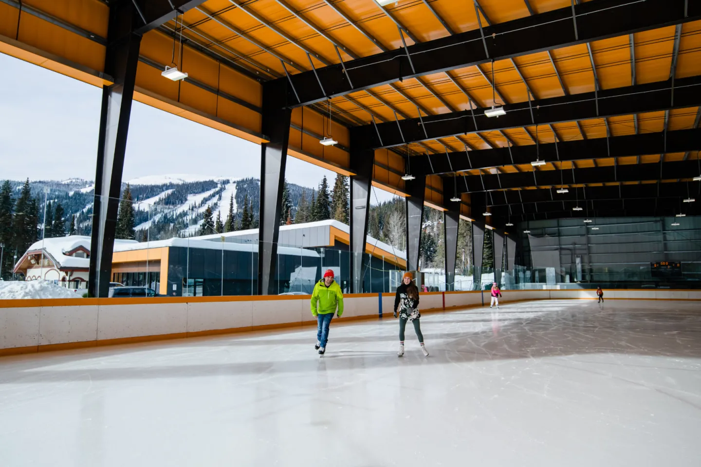 Two people skating on the rink with mountains behind them