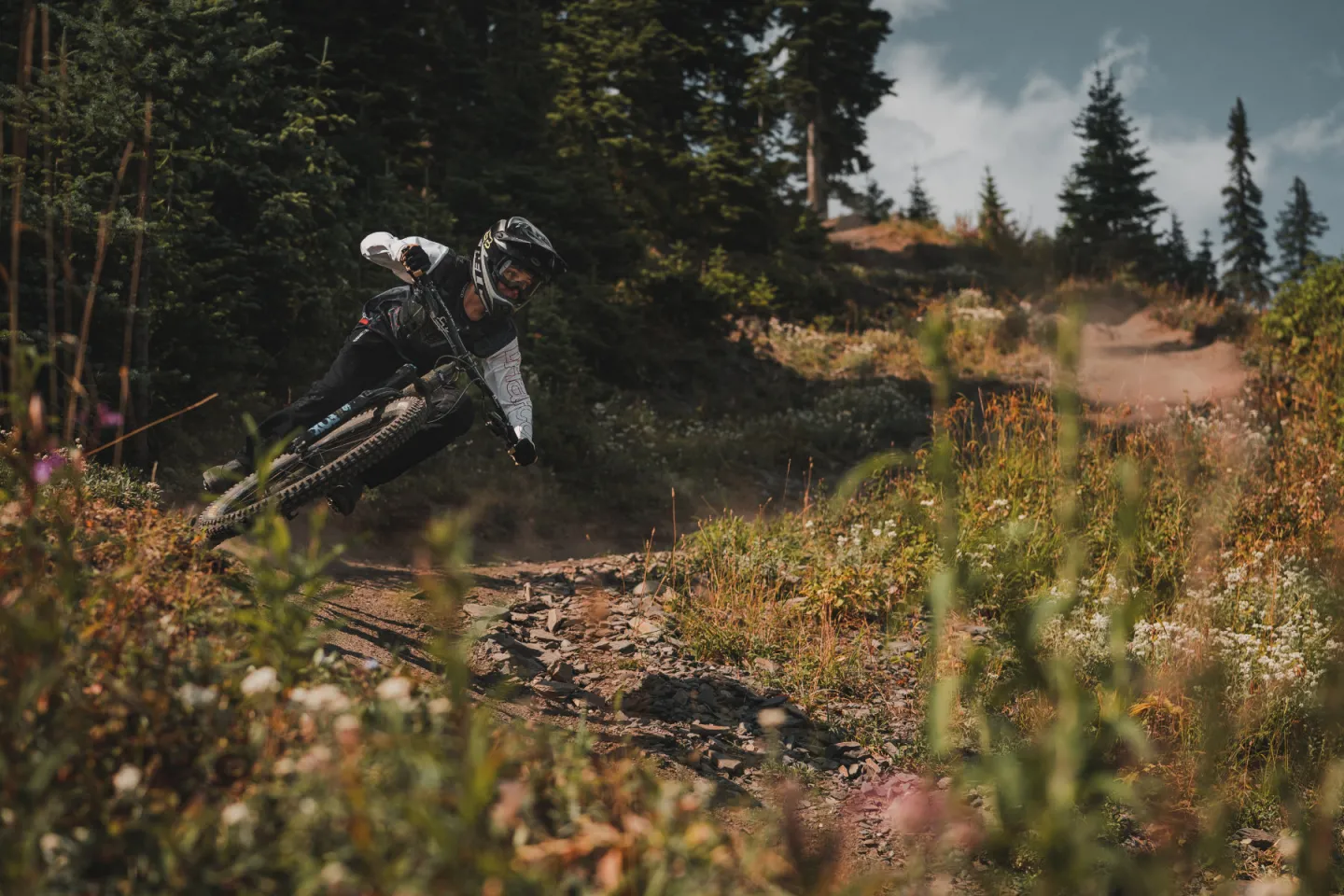 Downhill biker riding down a trail with trees in the background