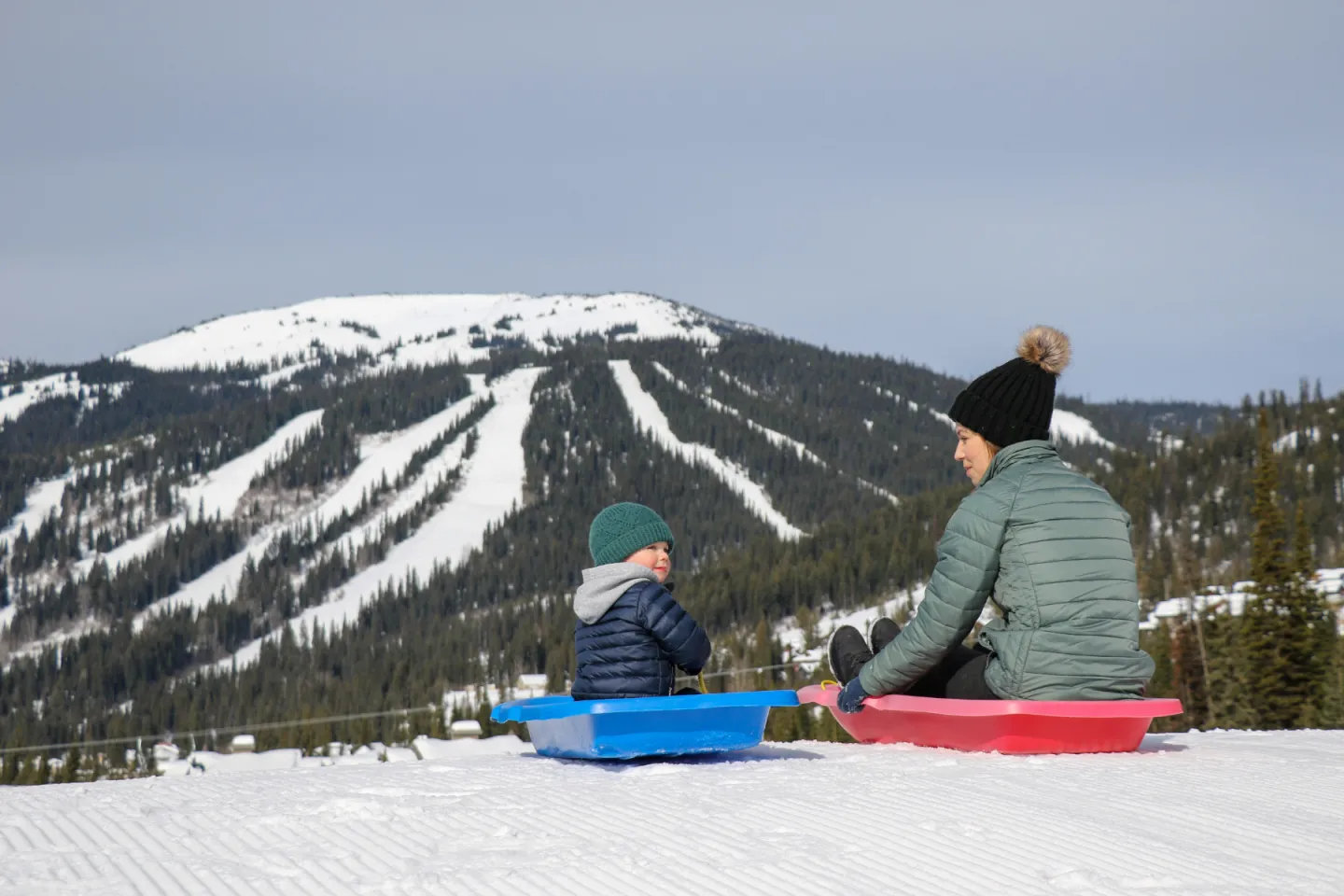 Two people sitting on a toboggan with a mountain in the background