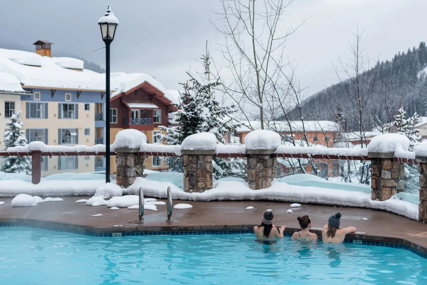 Three people in the outside pool with snowy buildings infront of them