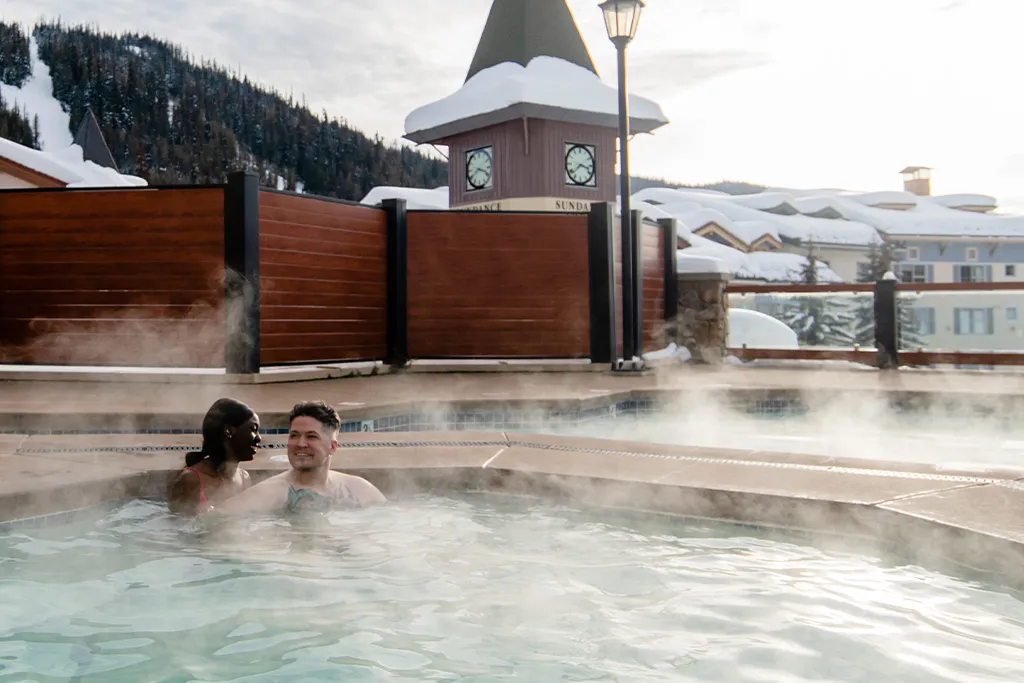 Two people in the outdoor pool with snowy mountains in the background