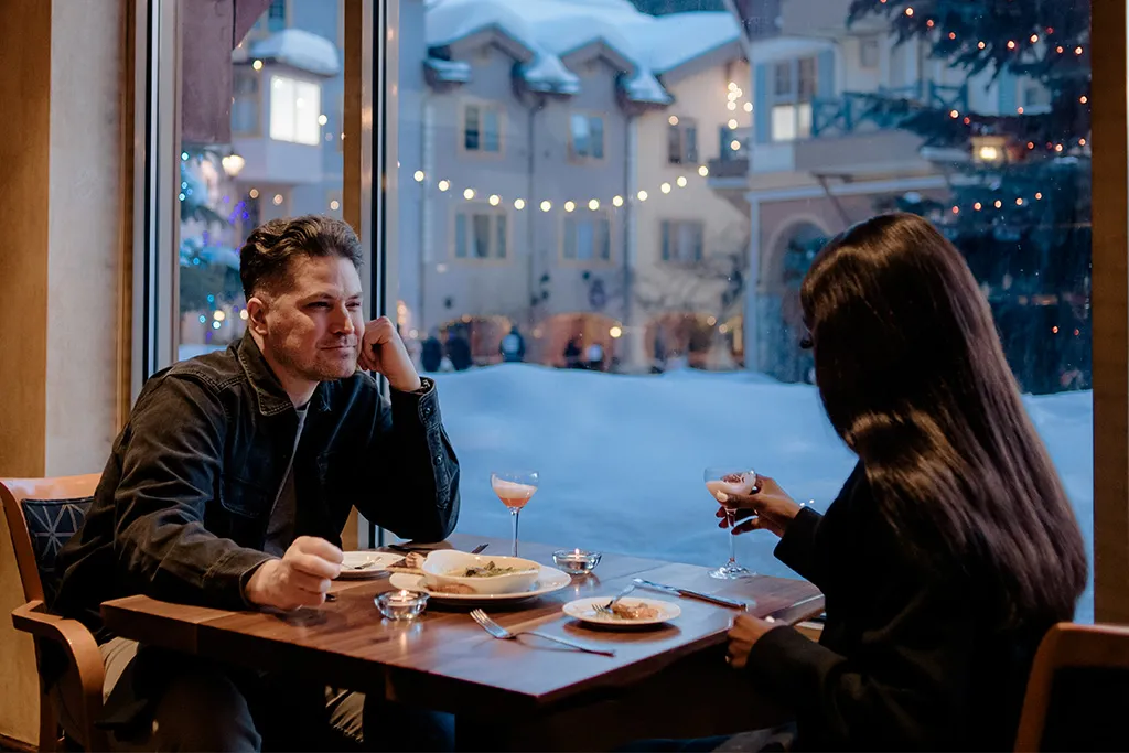 Two people sitting at a table drinking wine with the village in the background