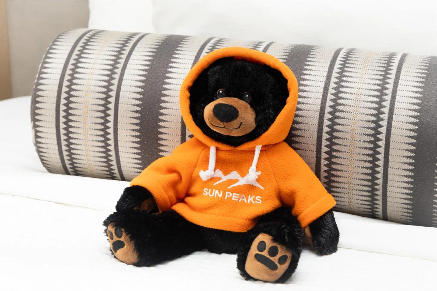 Teddy bear in an orange hoodie sitting on a bed.