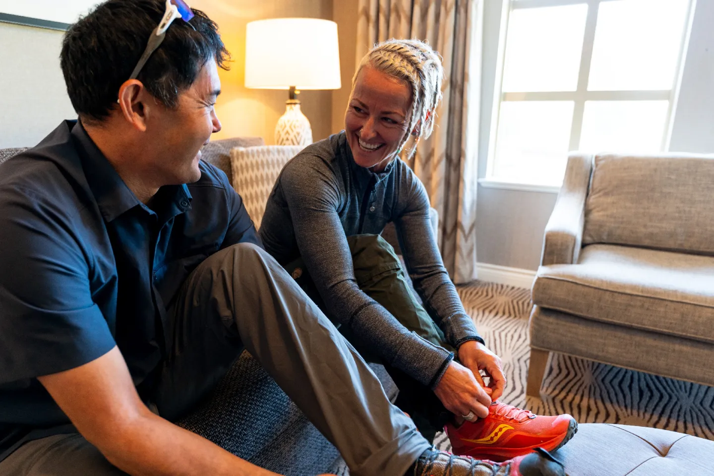 Two people sitting on a couch, smiling and chatting indoors.