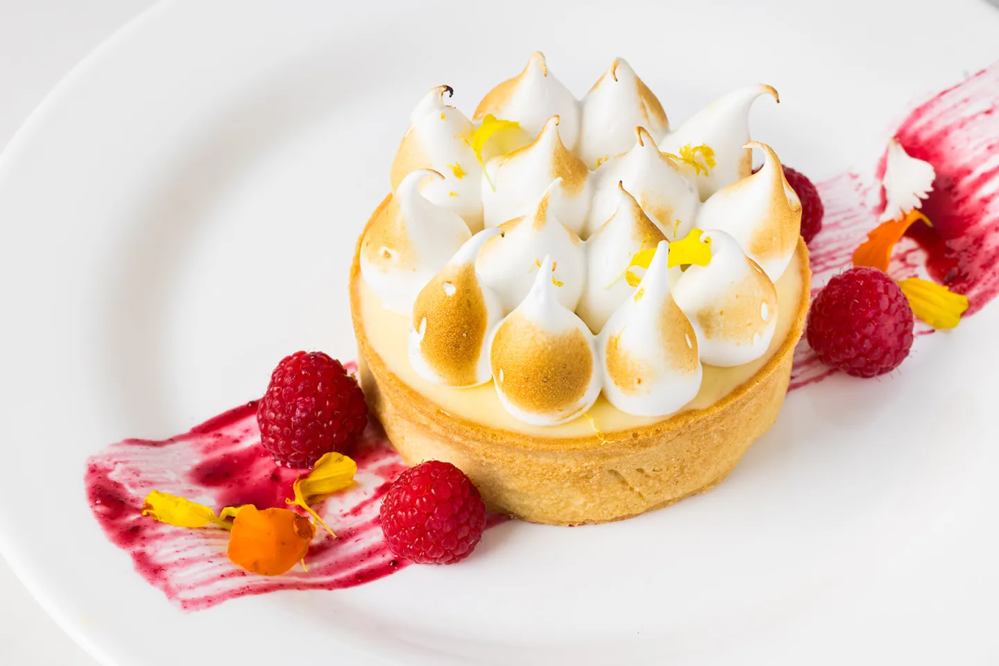Lemon meringue tart garnished with raspberries on a white plate.