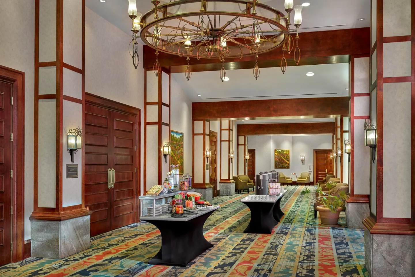 Spacious hallway with colorful carpet, large chandelier, and tables with refreshments.