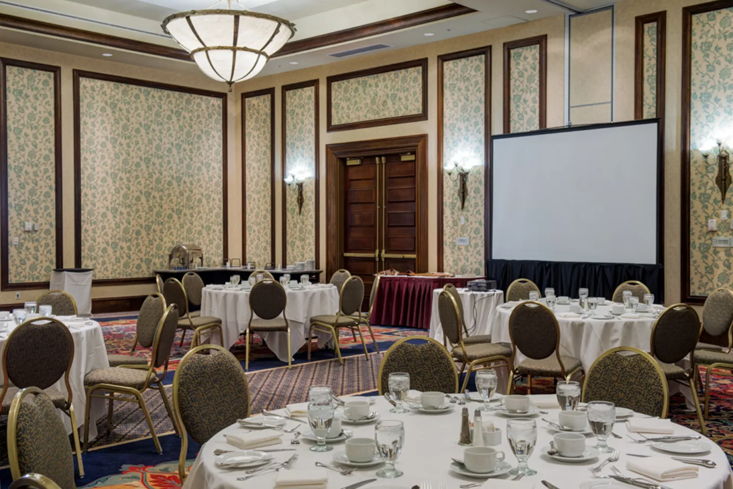 Banquet hall with round tables, white tablecloths, and a large projector screen.
