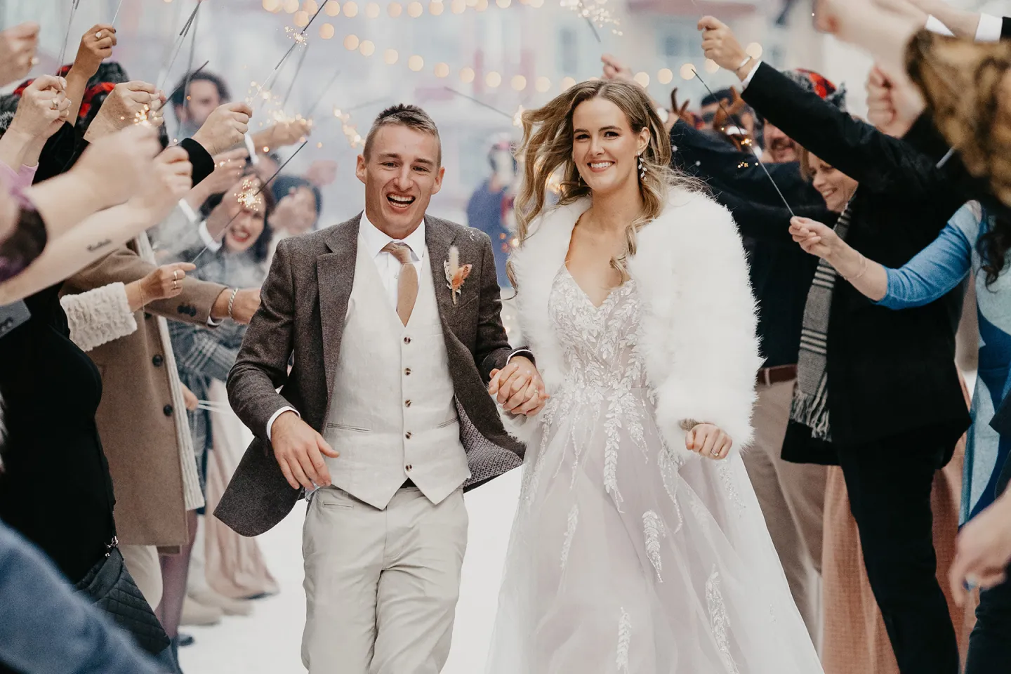 Bride and groom joyfully walk through cheering crowd with sparklers.