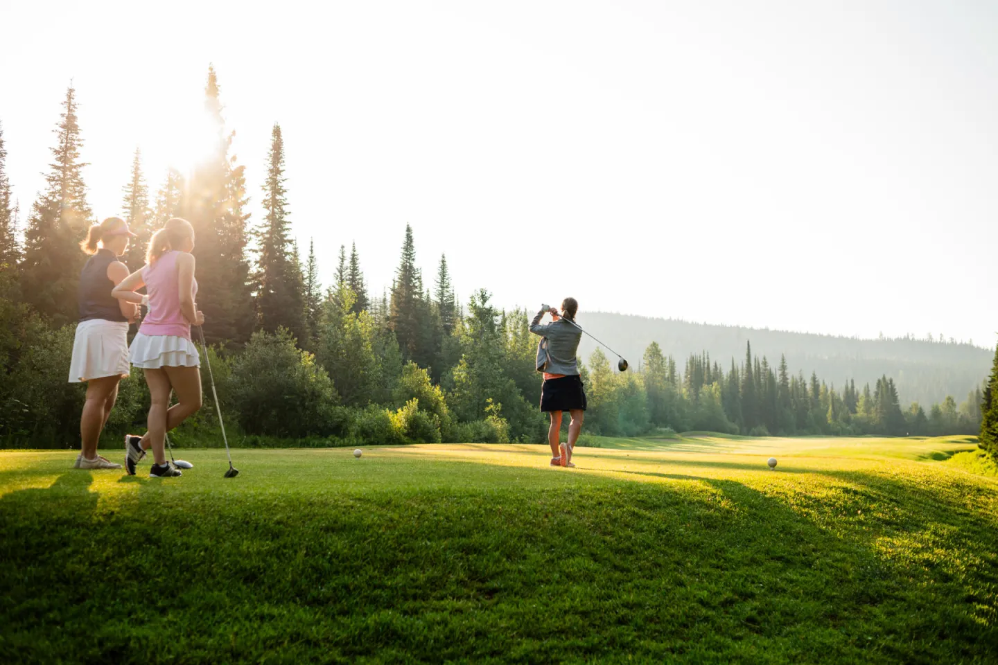 Golfers on a lush course with a forested backdrop.