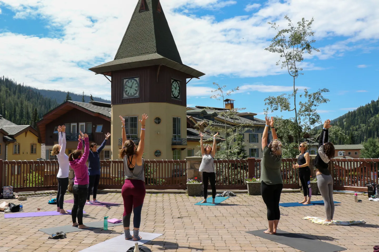 Outdoor yoga class with people stretching, mountains and buildings in the background.