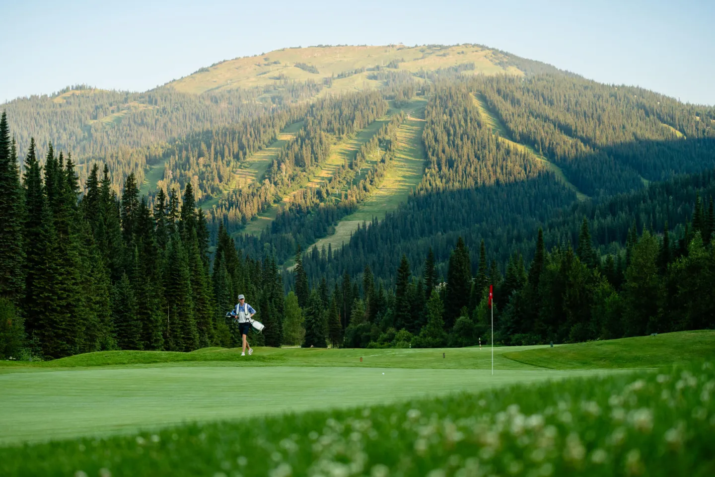 Golfer walking on a lush course with a mountain backdrop.