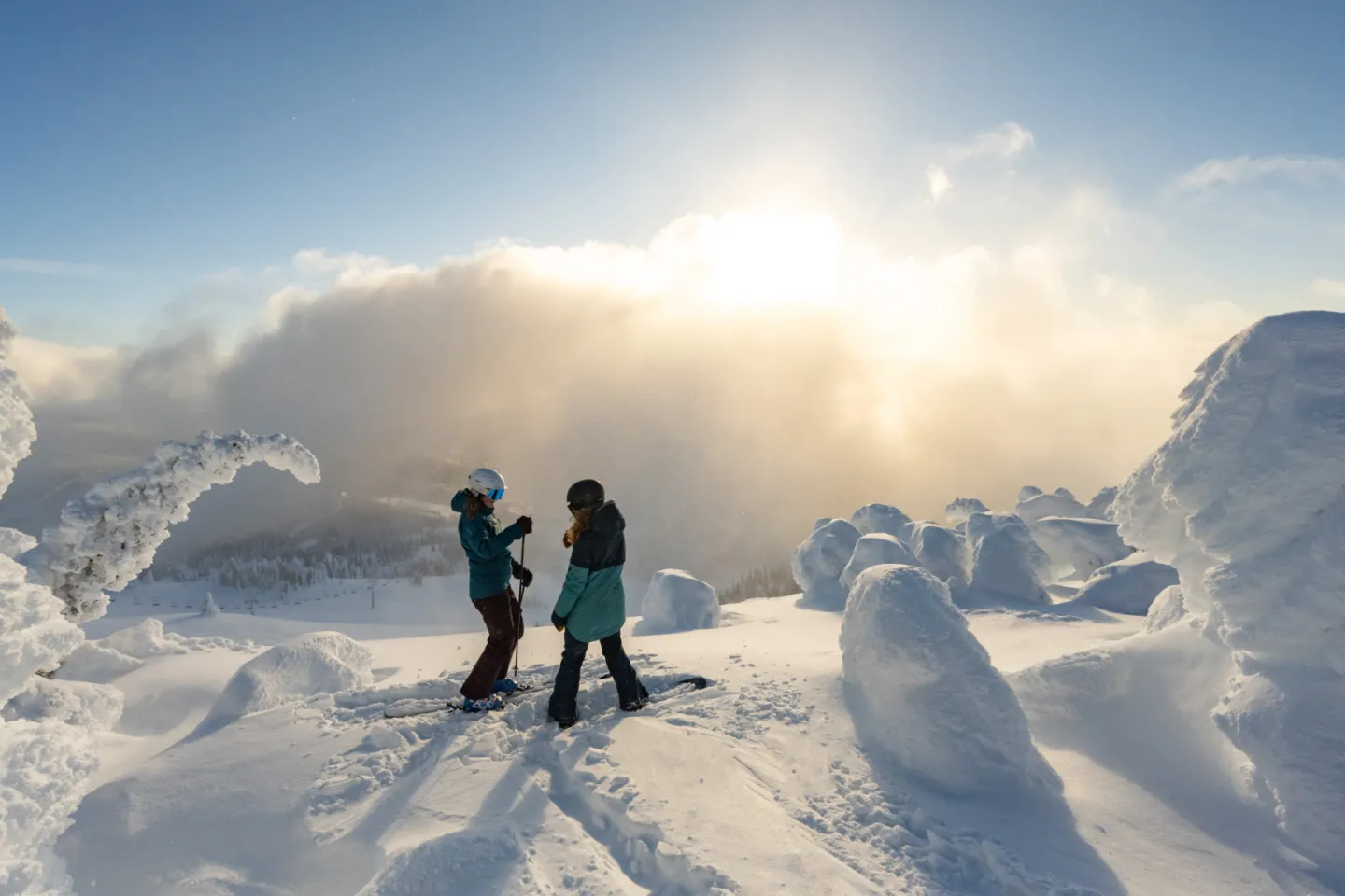 Two people in snow gear stand on a snowy landscape under a bright sun.