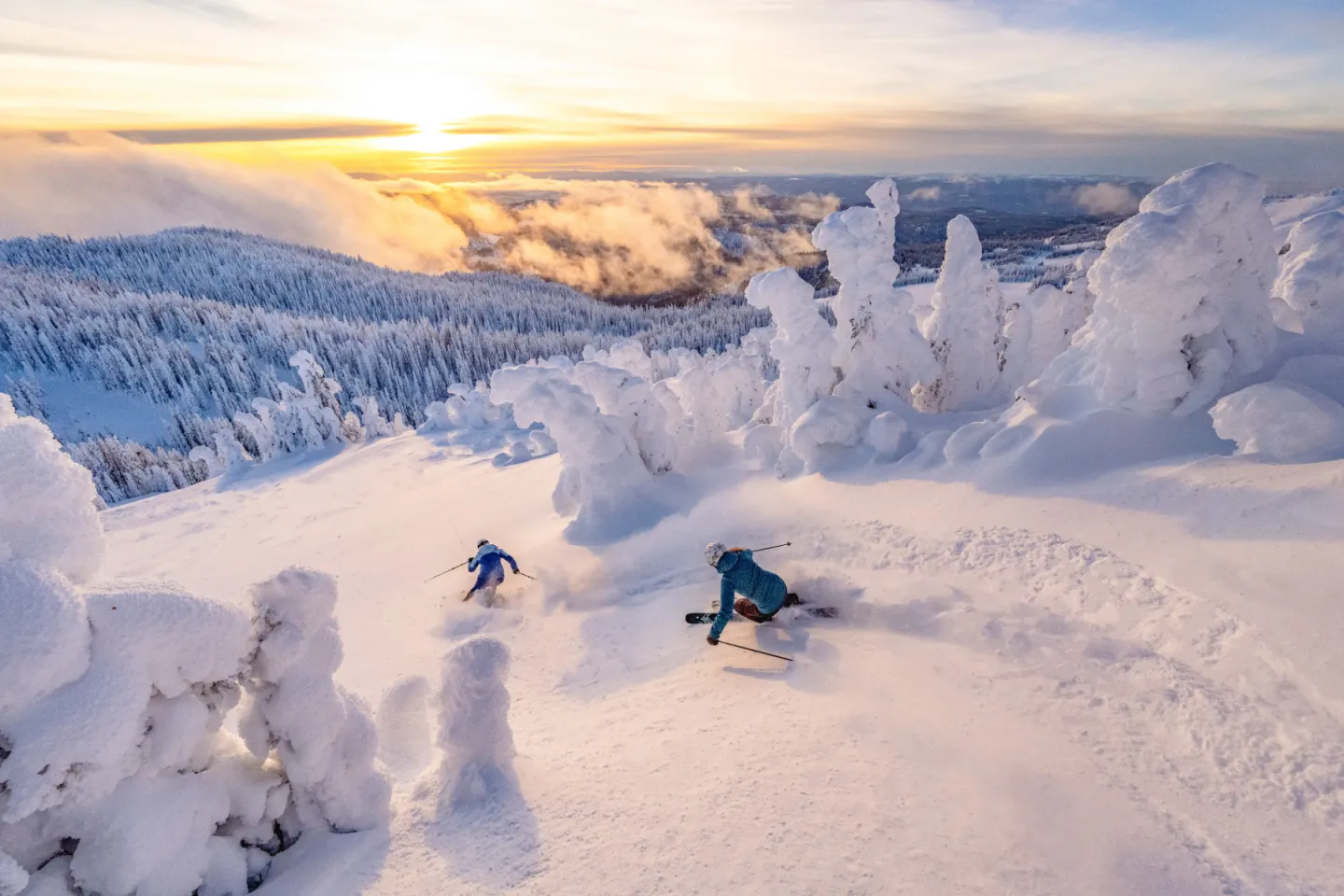 Skiers on a snowy slope at sunset with frosty trees.