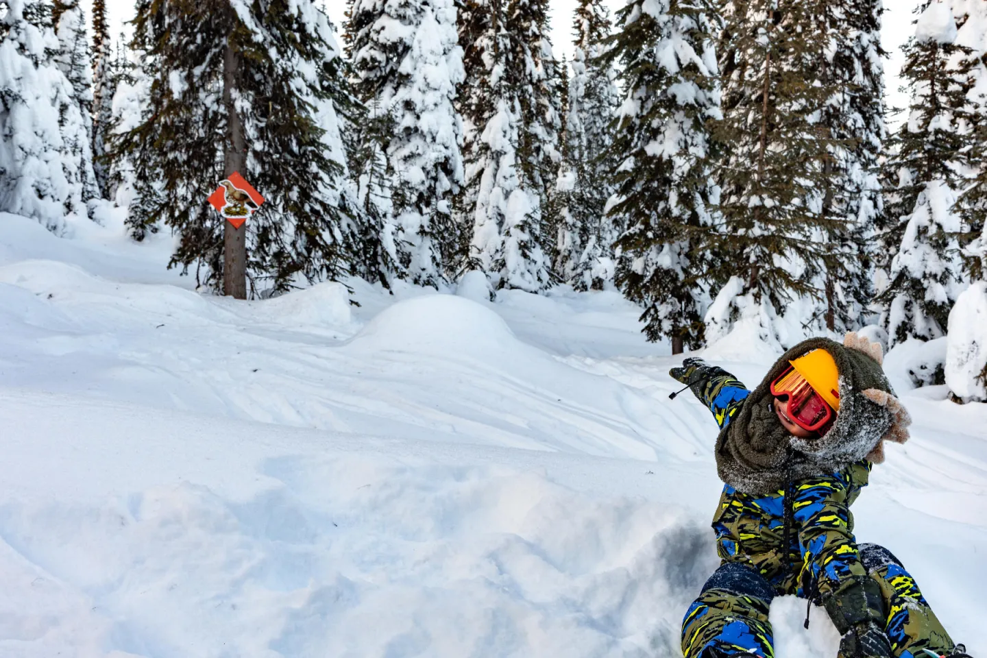 Child in snow gear playfully points in snowy forest.