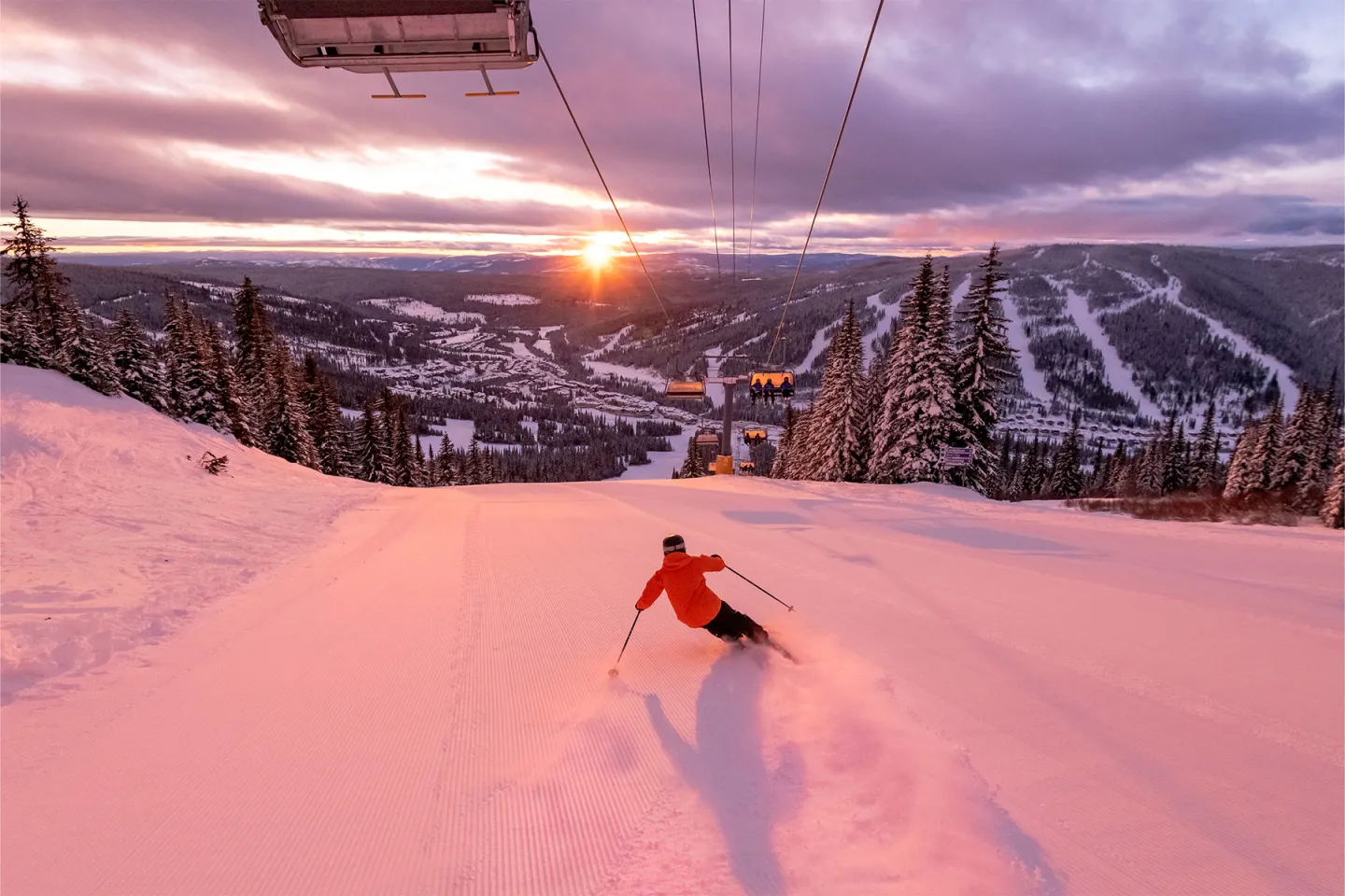 Skier in red descending snowy slope at sunset, scenic mountain view.