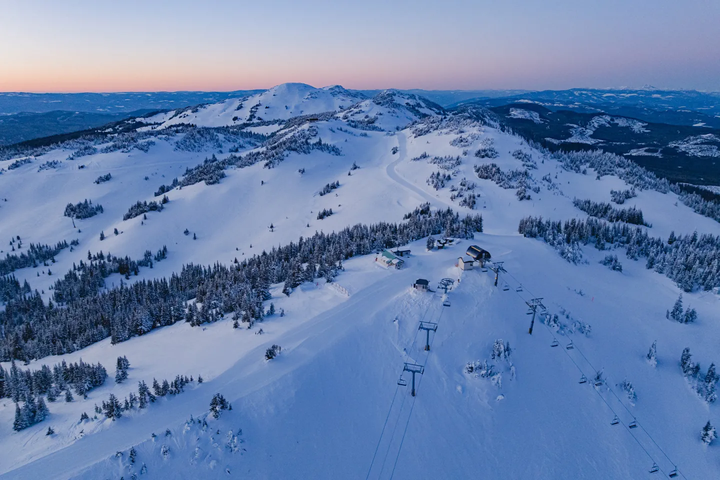 Snowy mountain landscape at twilight with ski lifts and distant peaks.