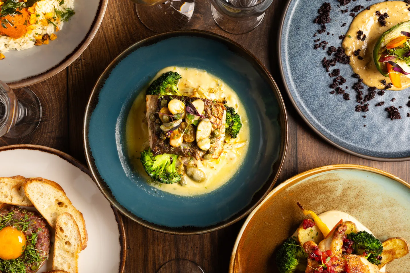 Elegant plates of gourmet dishes with colorful sauces and vegetables on a wooden table.