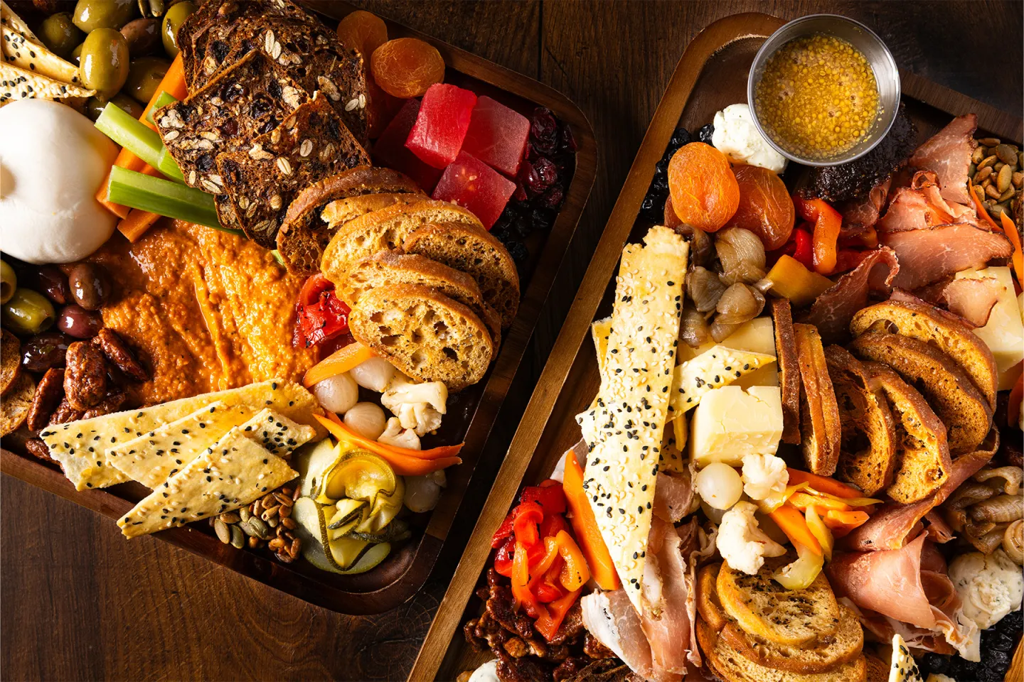 Two charcuterie boards with meats, cheeses, crackers, fruits, and a honey dip.