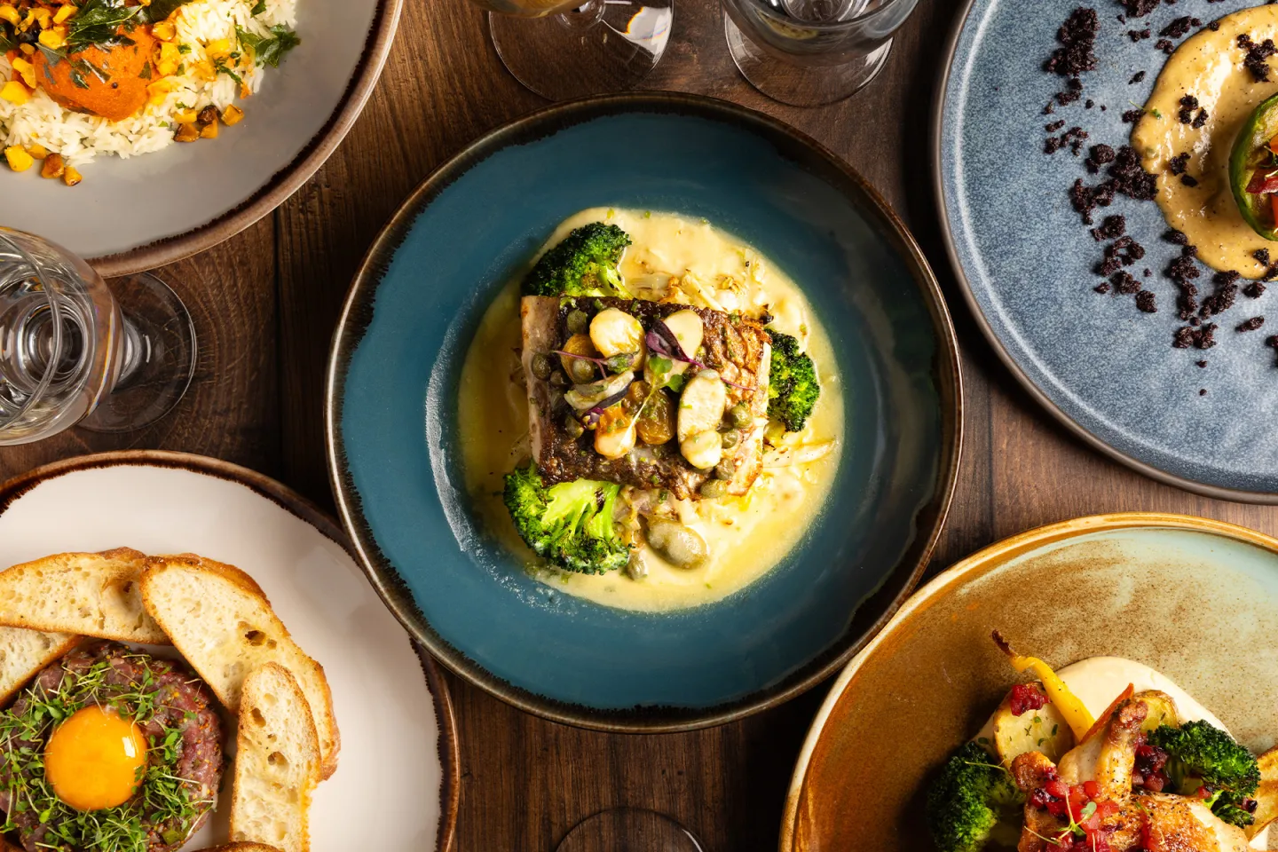 Variety of gourmet dishes on ceramic plates, arranged on a wooden table.