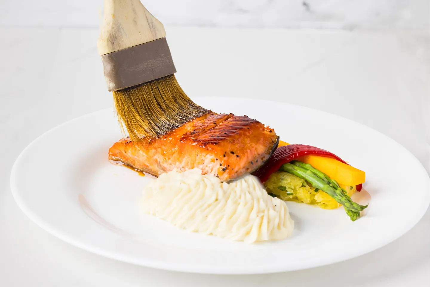 Grilled salmon with mashed potatoes and vegetables, being glazed with a brush.