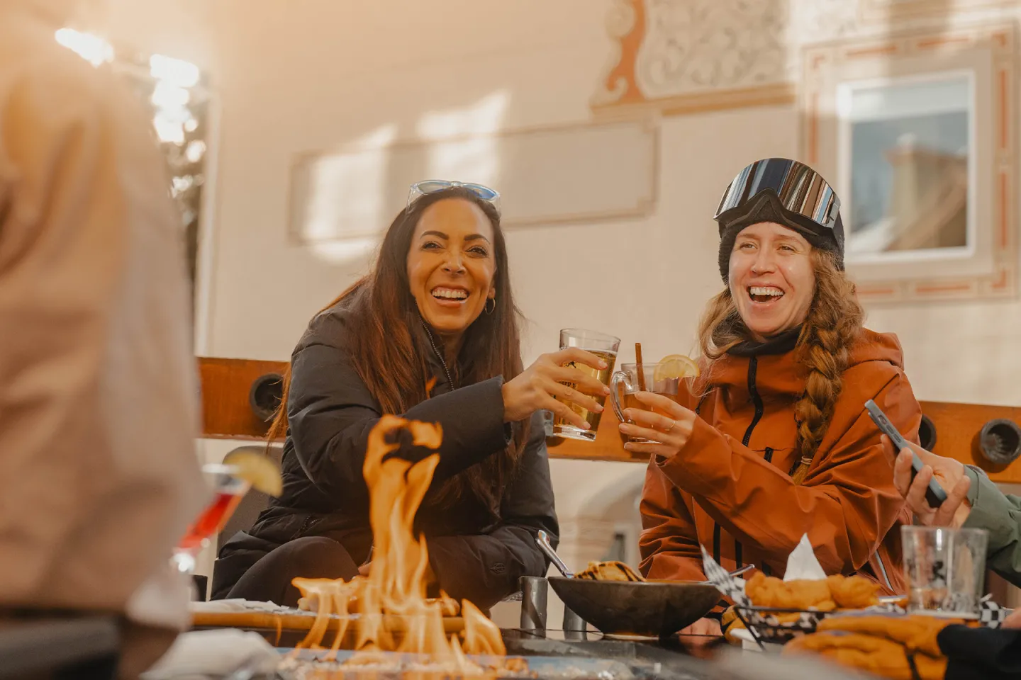Toasting women smiling around a fire pit outdoors.