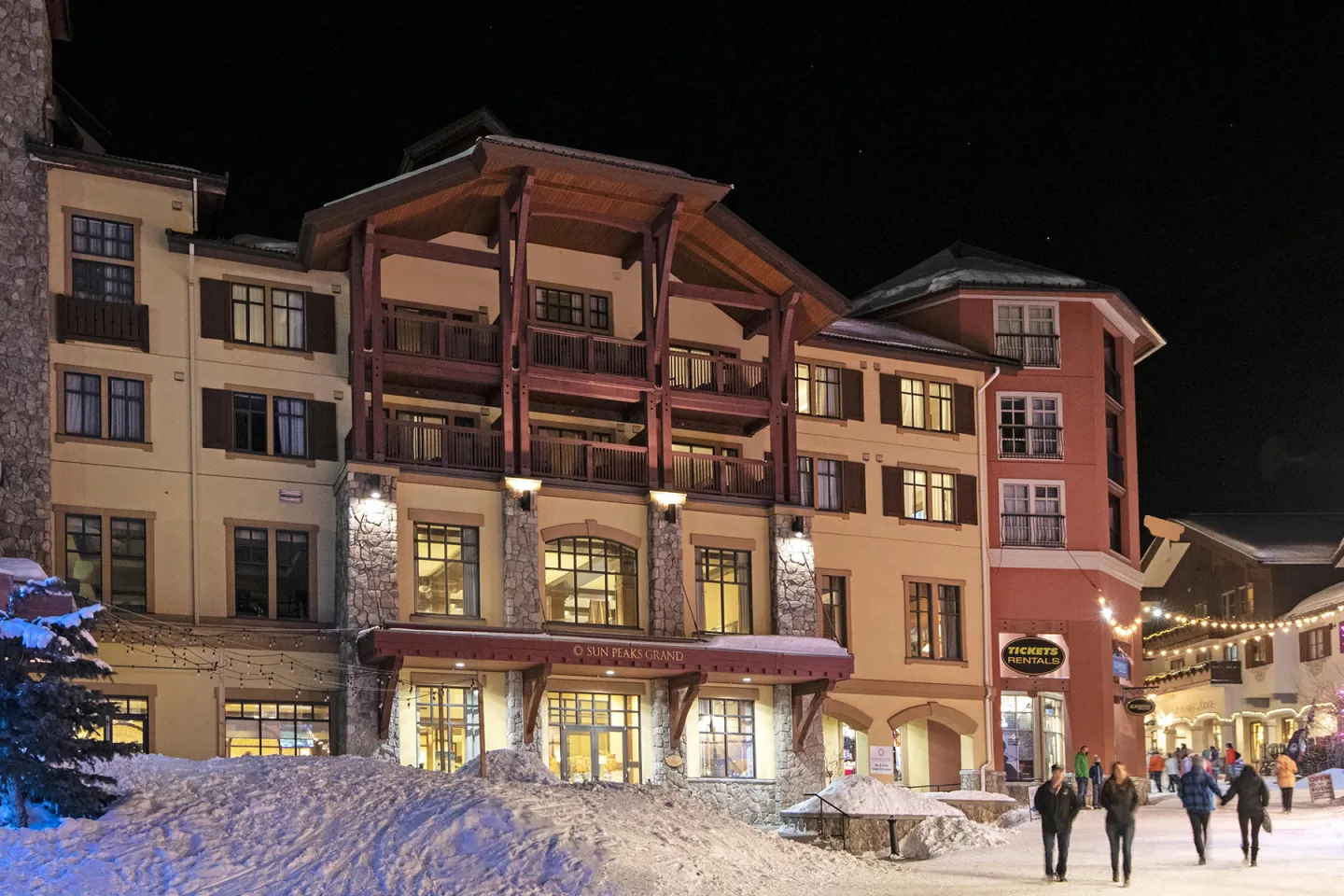 Ski resort buildings at night, warmly lit with snow in the foreground.