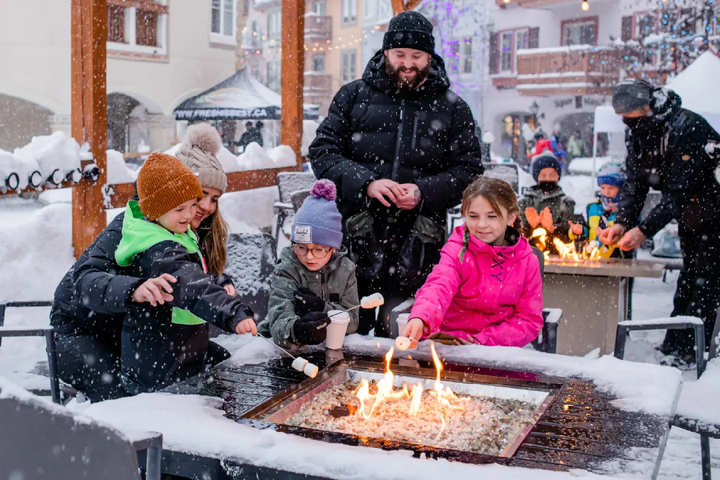 Children toast marshmallows over a firepit in a snowy outdoor setting.