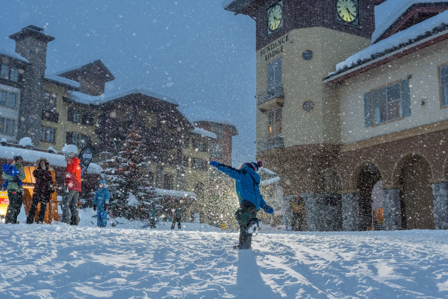 Child joyfully playing in a snowy village under a cloudy sky.