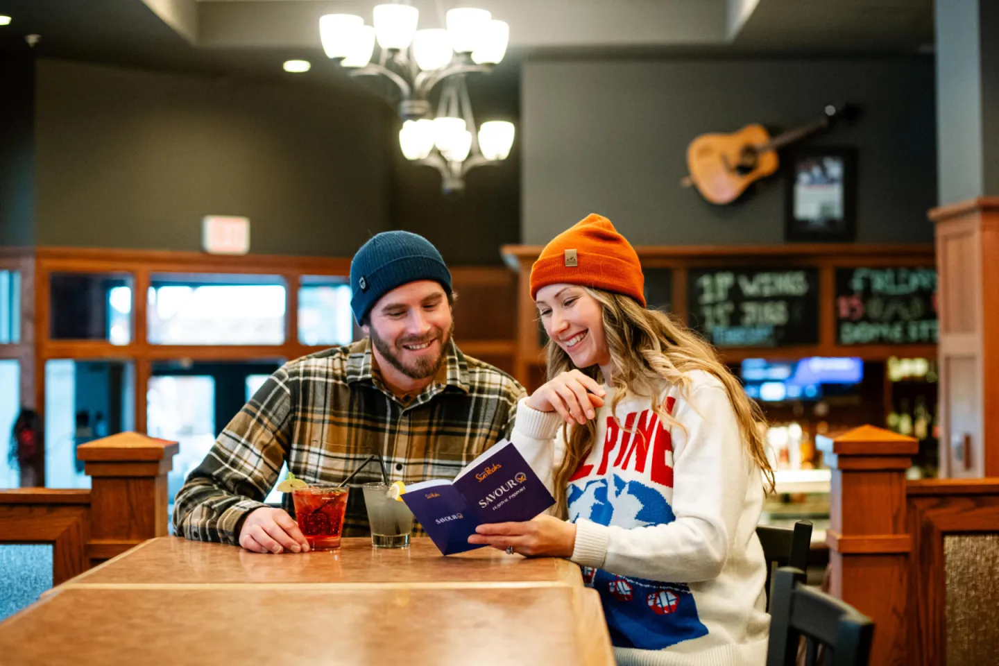 Two people in beanies read a menu at a cozy café table.
