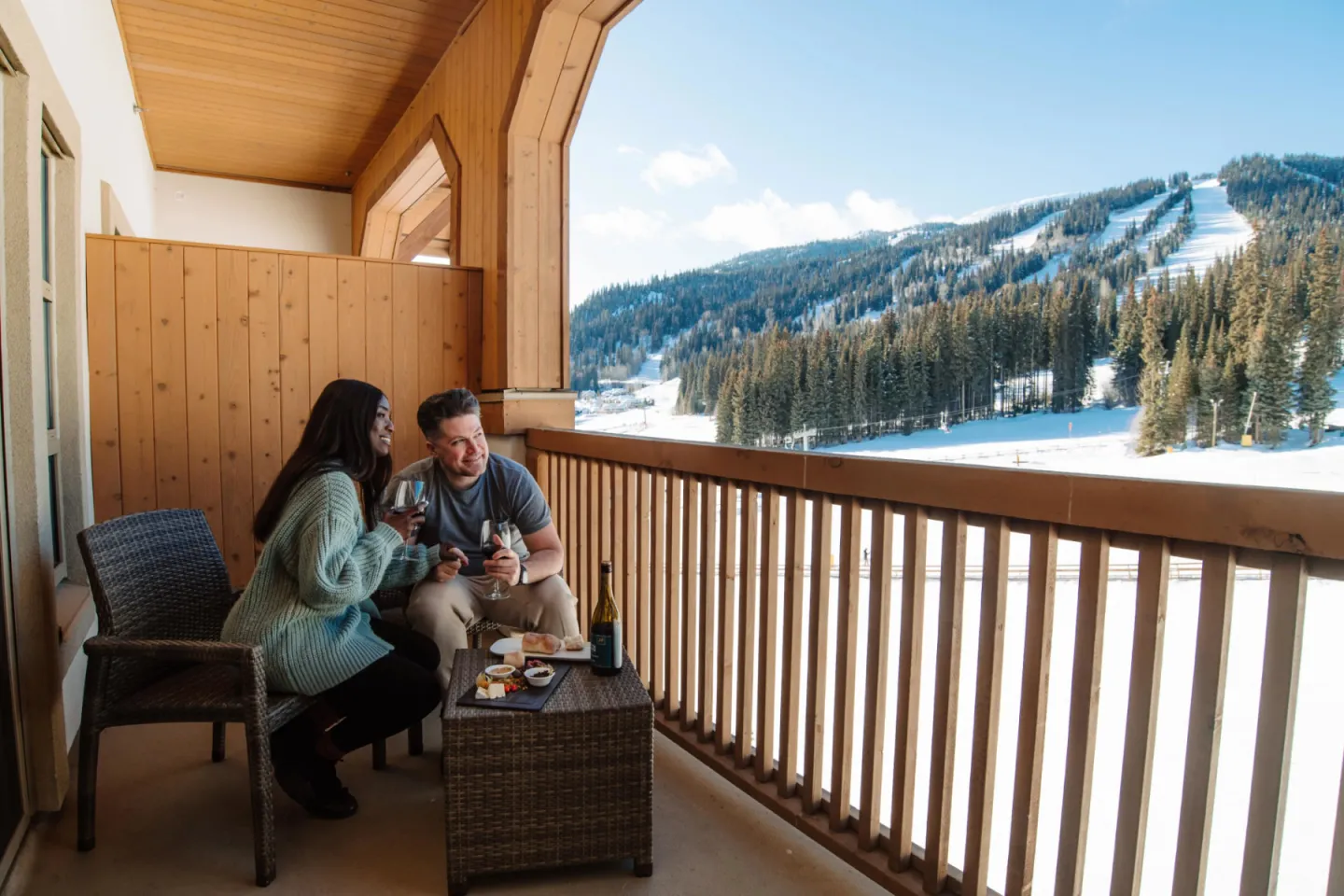 Couple on a balcony enjoying snacks with snowy mountain view.